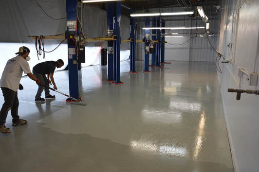 Two man coating the floor to give more design on the facility using a materials for epoxy flooring.